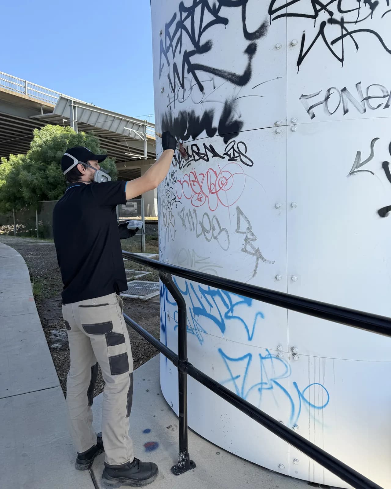 Kodi wearing a respirator, removing marker tags from a painted metal tank by hand