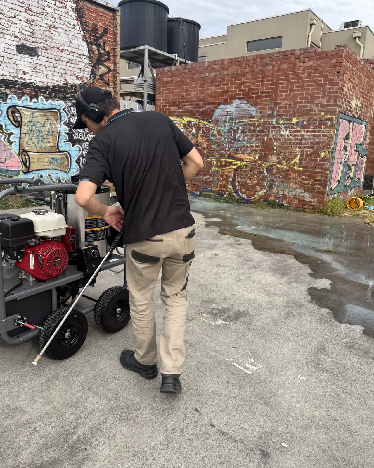 Kodi setting up a trolley-mounted hot water pressure unit in a laneway